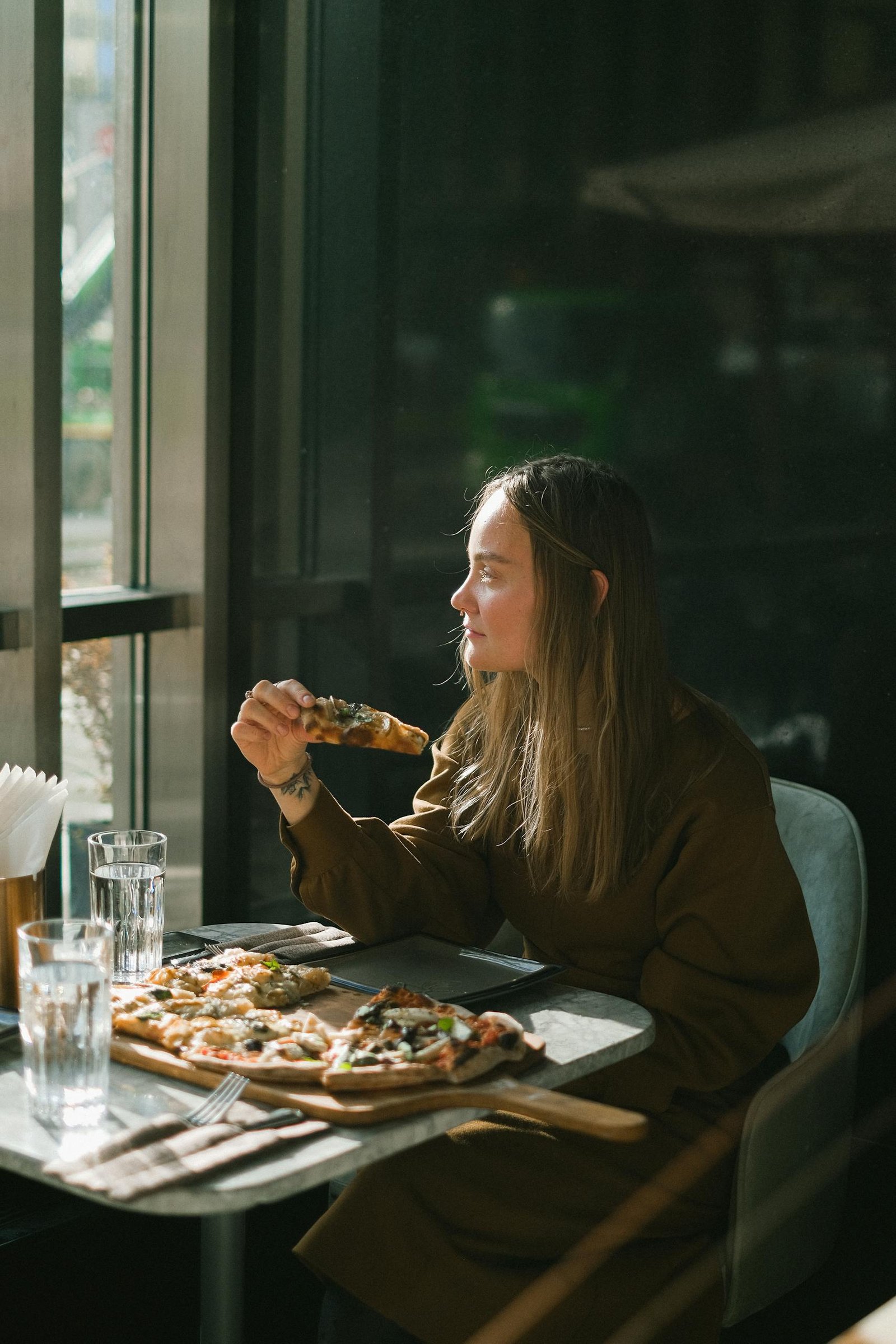 A woman enjoys a pizza at a sunlit restaurant table, surrounded by warm and cozy ambiance.